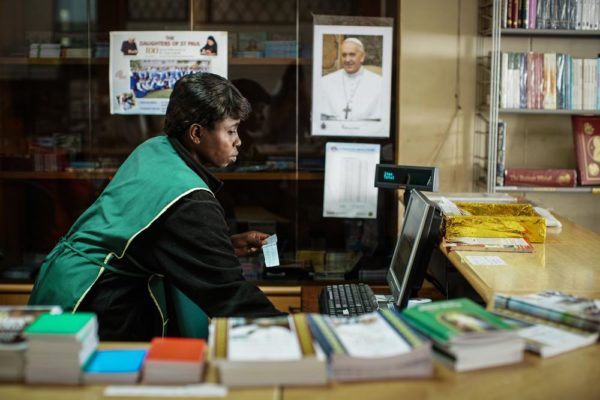 NAIROBI, KENYA - NOVEMBER 24: A cashier from the bookstore at the Holy Family Basilica prints a receipt in front of a poster of Pope Francis on November 24, 2015 in Nairobi, Kenya. Pope Francis makes his first visit to Kenya on a five day African tour that is scheduled to include Uganda and the Central African Republic. Africa is recognised as being crucial to the future of the Catholic Church with the continent's Catholic numbers growing faster than anywhere else in the world. (Photo by Nichole Sobecki/Getty Images)