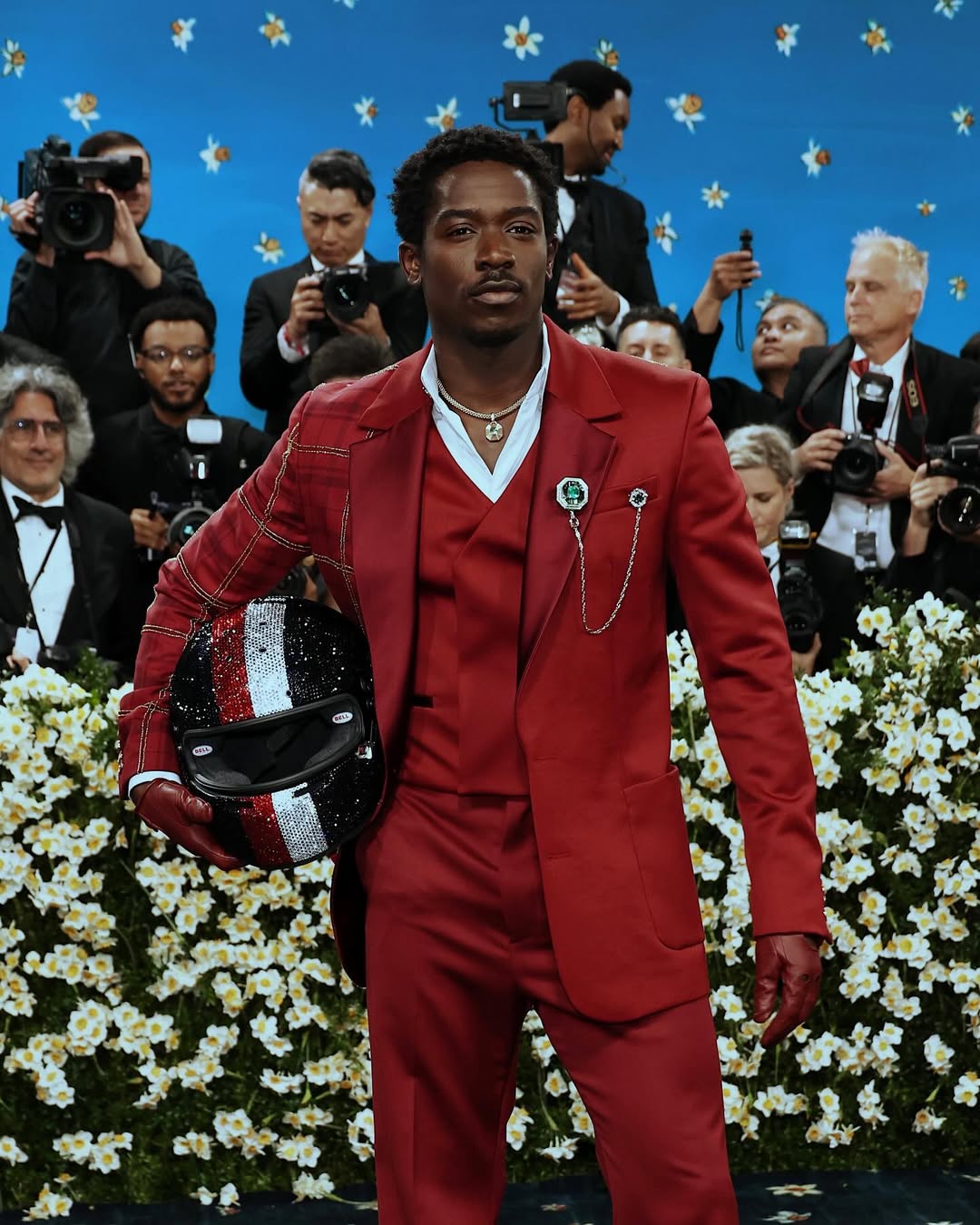 Actor Damson Idris at the 2025 Met Gala in NYC wearing a custom red Tommy Hilfiger tartan suit for the "Superfine: Tailoring Black Style" theme, holding a Swarovski-crystal-encrusted F1 helmet as a nod to his film Formula 1.