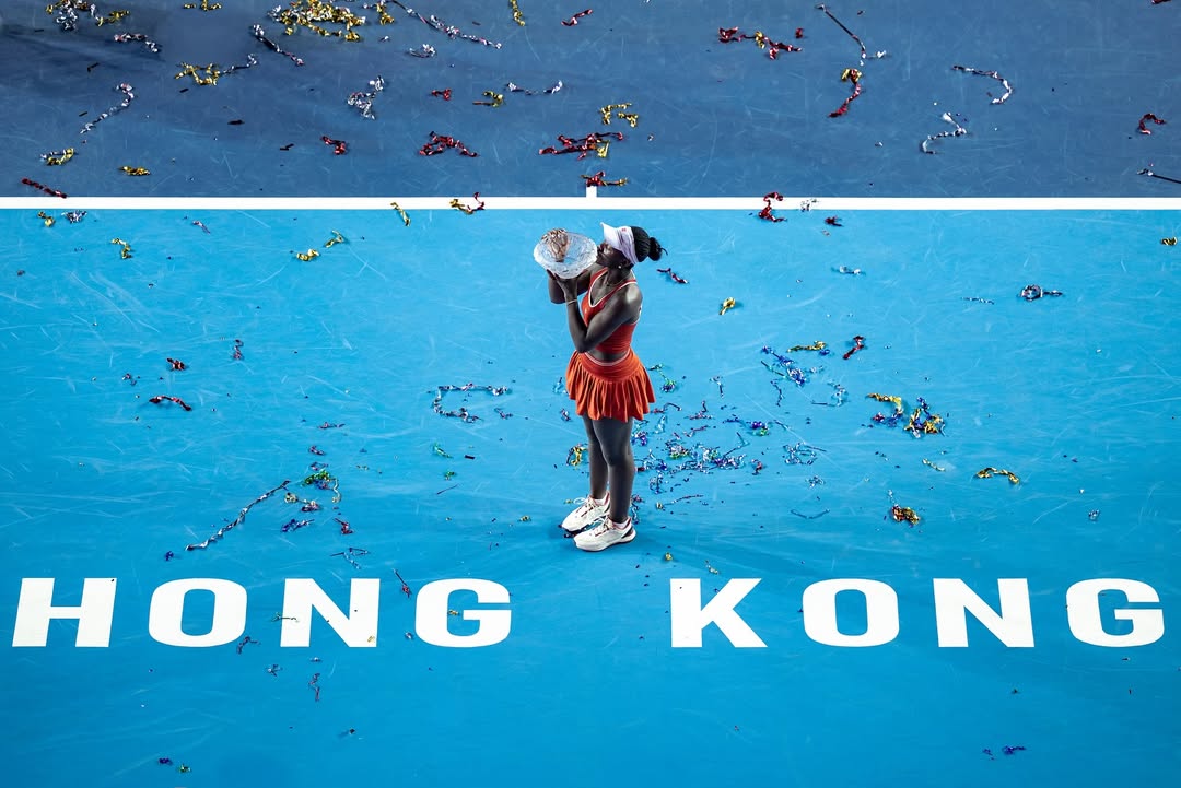 Victoria Mboko kissing the winner's trophy on the blue hard court at Victoria Park after winning the 2025 Hong Kong Open.