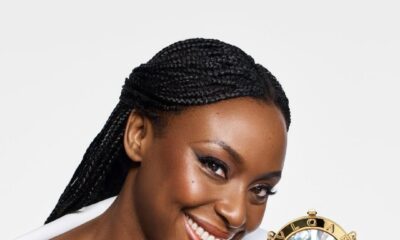 Chimamanda Ngozi Adichie wearing a structured white off-the-shoulder top and gold B.zero1 rings, posed with the circular gold BVLGARI BVLGARI Icons Minaudière and a stack of miniature books.