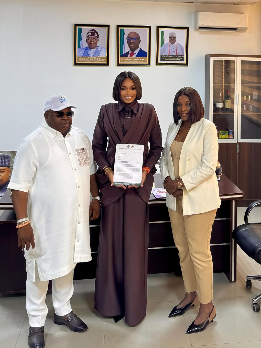 Sabrina Idukpaye standing with Commissioner Hon. Christopher E. Okaeben and Ministry official while holding her appointment letter.