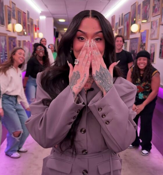 R&B singer Kehlani dancing through the Spirit Tunnel on The Jennifer Hudson Show. She is wearing a grey oversized belted blazer, a matching mini skirt, and burgundy tights, surrounded by the show's cheering crew.