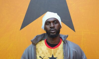 Ghanaian musician Black Sherif wearing the 2026 yellow Ghana away jersey with a grey jacket and white beanie.