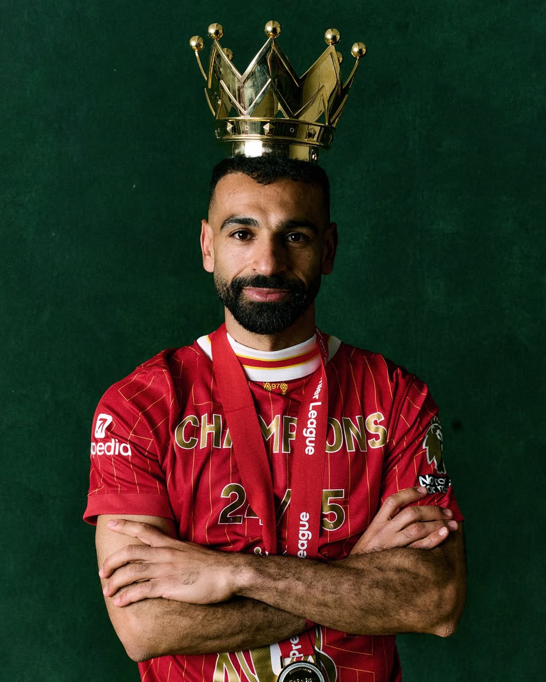 A close-up studio portrait of Mohamed Salah in the Liverpool home kit, capturing his focused "Egyptian King" expression.