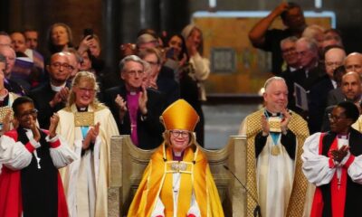 Dame Sarah Mullally seated on the Archbishop's throne in Canterbury Cathedral surrounded by clergy.