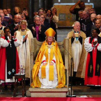 Dame Sarah Mullally seated on the Archbishop's throne in Canterbury Cathedral surrounded by clergy.
