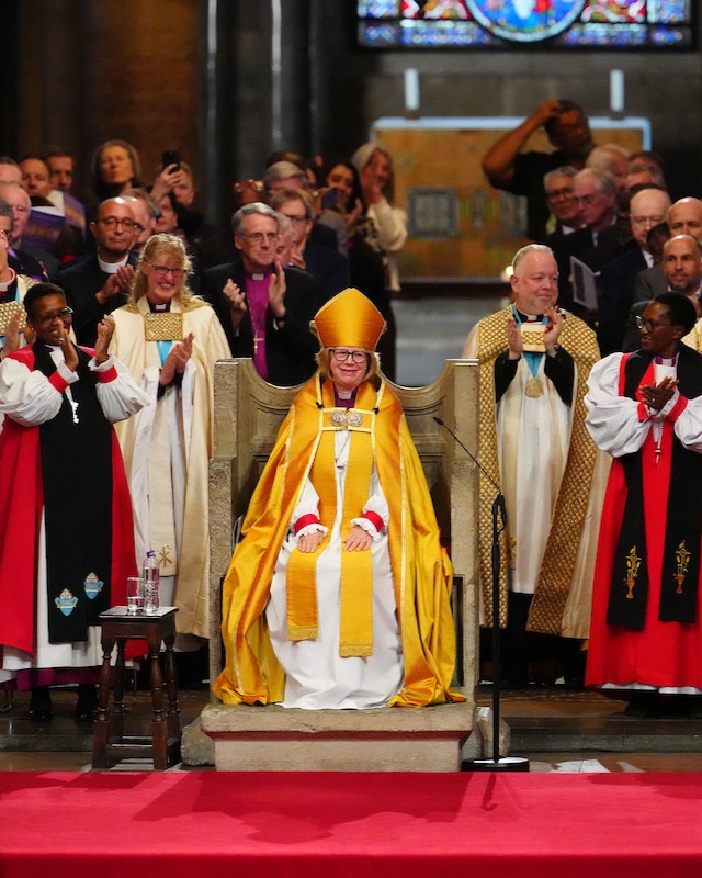Dame Sarah Mullally seated on the Archbishop's throne in Canterbury Cathedral surrounded by clergy.
