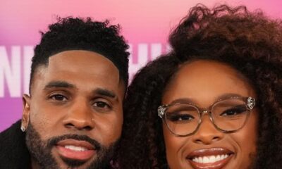 A close-up portrait of Jason Derulo in a black coat and Jennifer Hudson in a red outfit smiling together.
