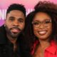 A close-up portrait of Jason Derulo in a black coat and Jennifer Hudson in a red outfit smiling together.