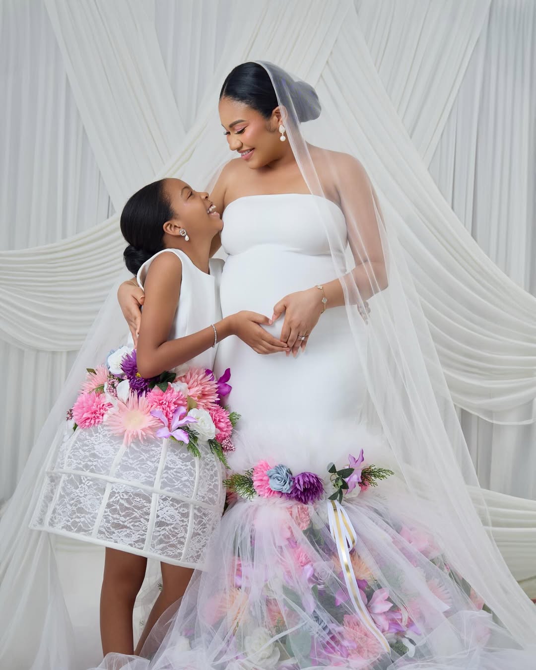 Anna Ebiere Banner in a white floral maternity gown with a sheer veil, posing with her daughter Sophia.