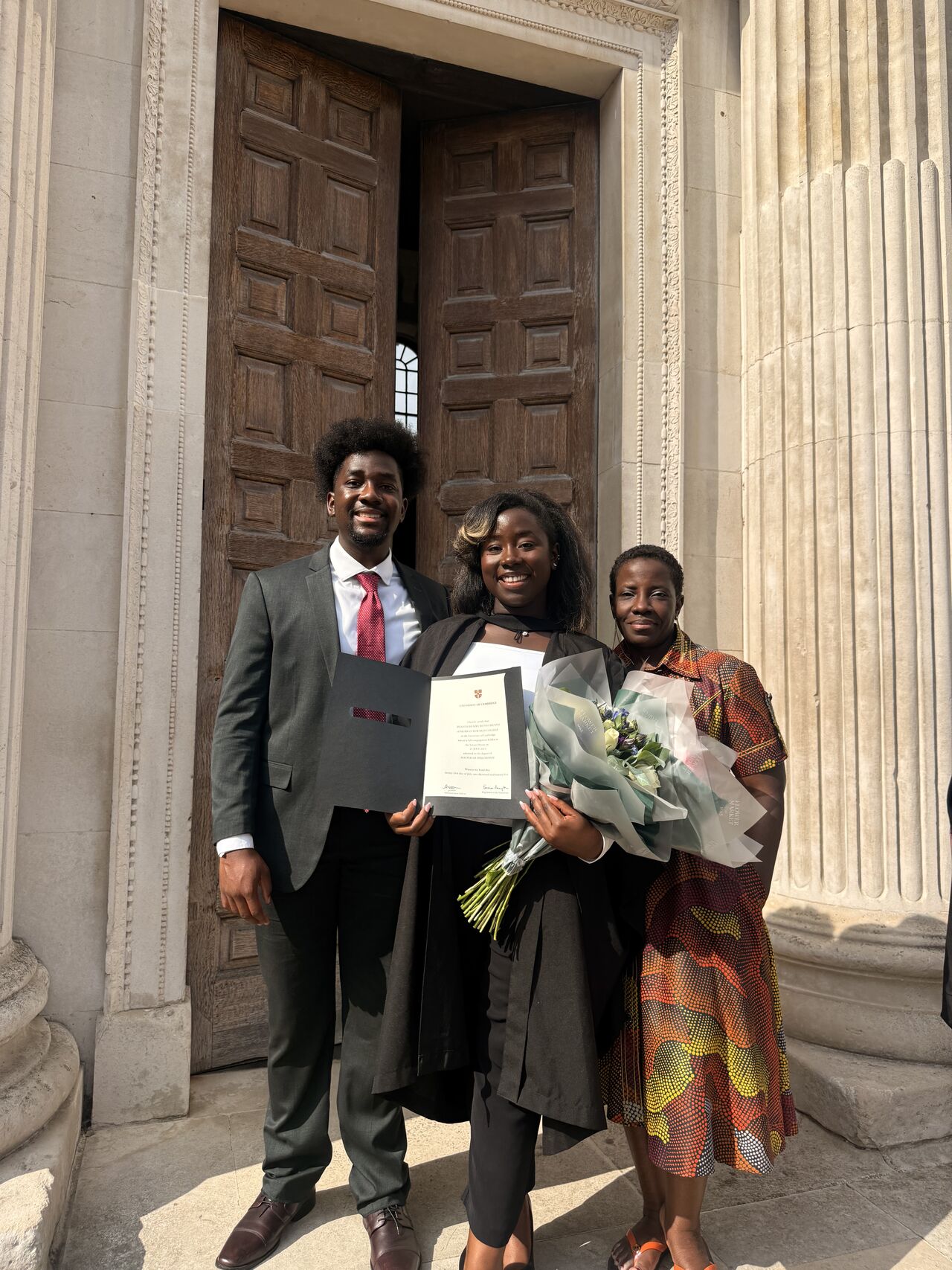 Ifeanyi Ruth Umunna in graduation robes holding her Cambridge diploma with Professor Dehlia Umunna and Edozie Umunna.