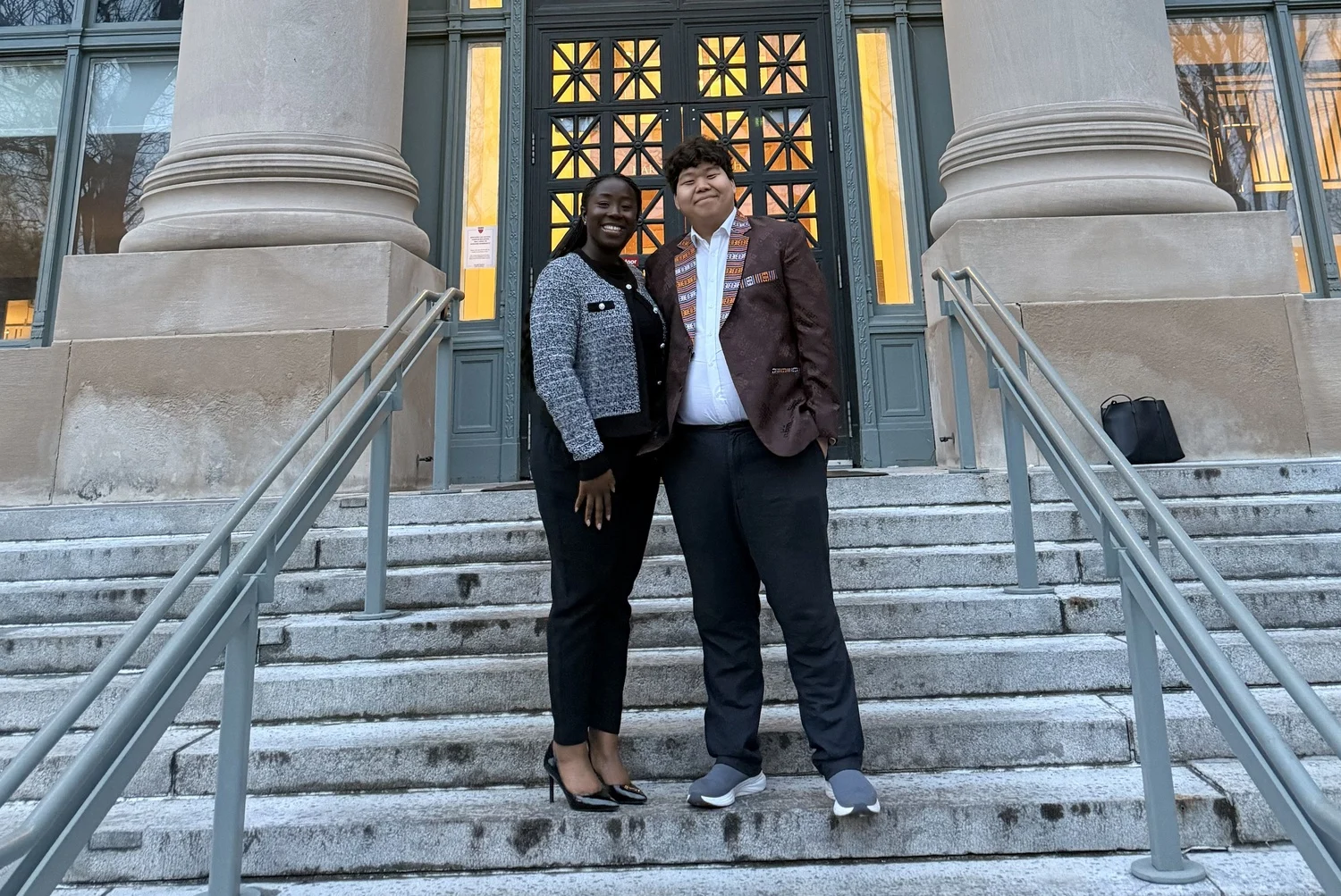 Ifeanyi Ruth Umunna and Tenzin Yonten standing together on the steps of a Harvard Law School building after being elected Co-Presidents.