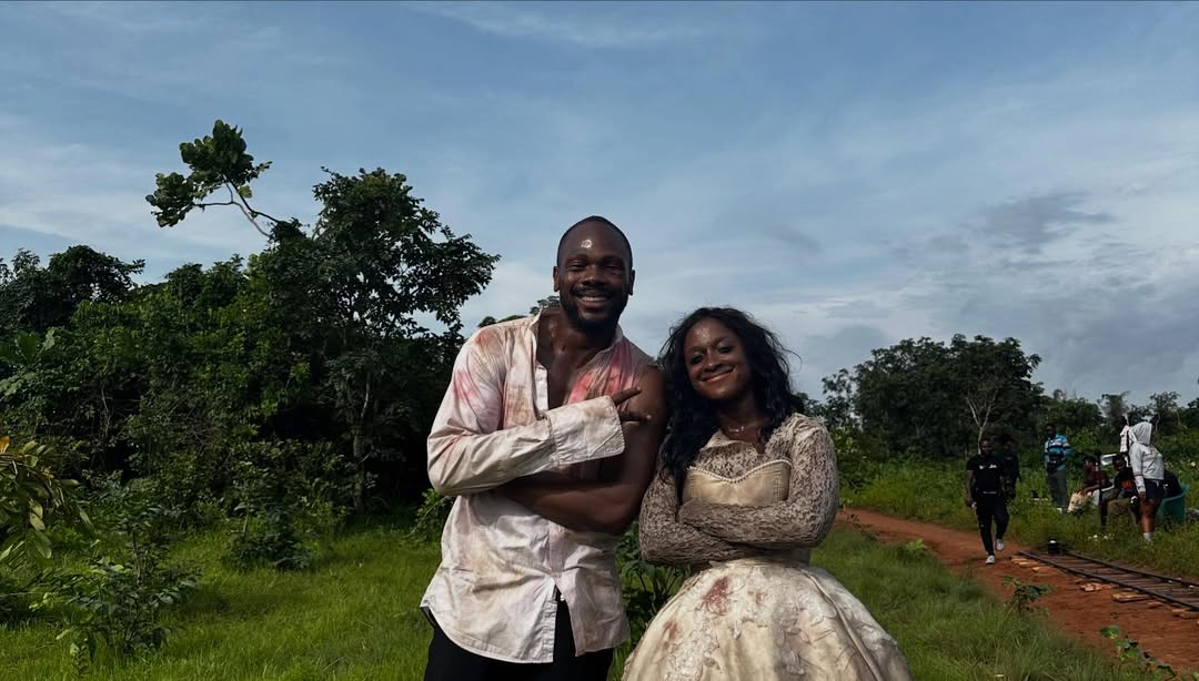 Director Daniel Etim Effiong and actress Genoveva Umeh (as Derin) posing together on the outdoor set of The Herd, both appearing in character with distressed clothing.