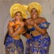 Funke Akindele and Iyabo Ojo laughing in coordinated blue and gold traditional lace outfits with elaborate yellow geles for the film Behind The Scenes.