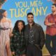 Halle Bailey and Regé-Jean Page posing together in front of a "You, Me & Tuscany" movie poster featuring them in a romantic Italian setting.
