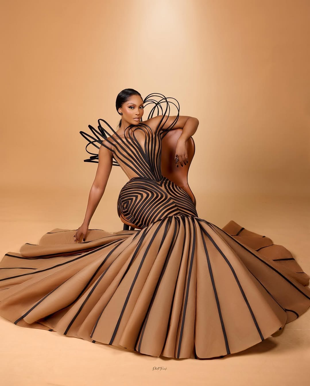 Osas Ighodaro at the 2024 AMVCA in a sculptural caramel and black geometric mermaid gown by Veekee James with a looping wire collar.