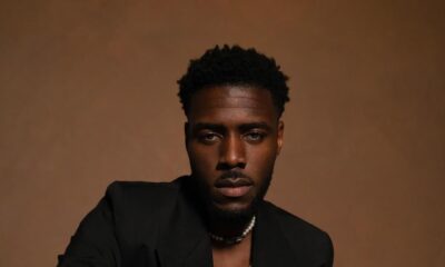 Actor Tega Alexander, who joins Bridgerton Season 5 as Christopher Anderson, posing in a black tailored blazer and pearl necklace.