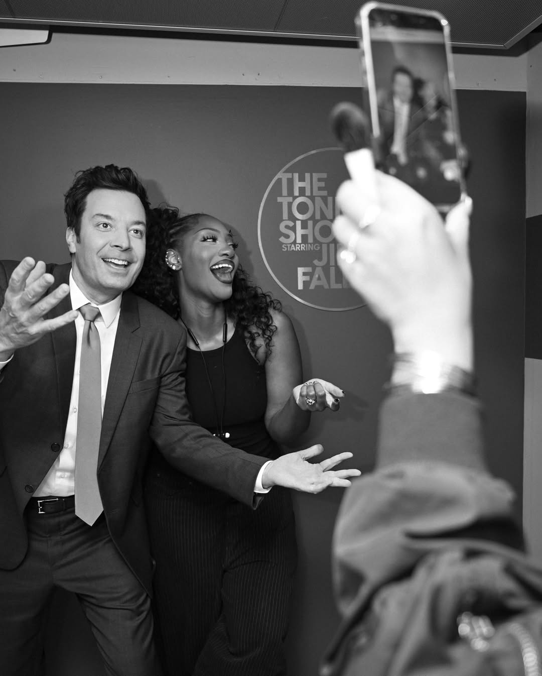 A black and white photo of Tems and Jimmy Fallon smiling and posing backstage at The Tonight Show.