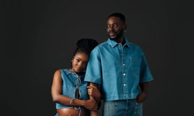 Singer Simi and her husband Adekunle Gold posing in matching mid-wash denim outfits. Simi is seated, wearing a lace-up denim crop top and wide-leg jeans, showing her baby bump. Adekunle stands beside her in a short-sleeved denim button-down and straight-leg jeans.