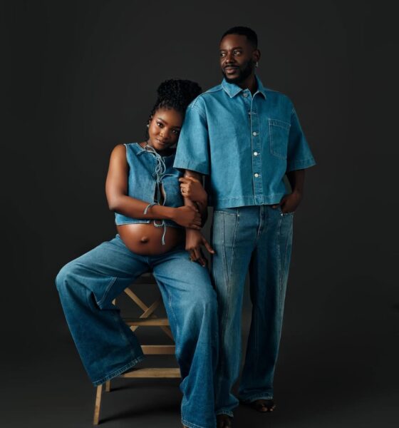 Singer Simi and her husband Adekunle Gold posing in matching mid-wash denim outfits. Simi is seated, wearing a lace-up denim crop top and wide-leg jeans, showing her baby bump. Adekunle stands beside her in a short-sleeved denim button-down and straight-leg jeans.