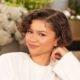 A close-up of Zendaya smiling during her interview on The Jennifer Hudson Show, wearing a structured white peplum top with fur trim.