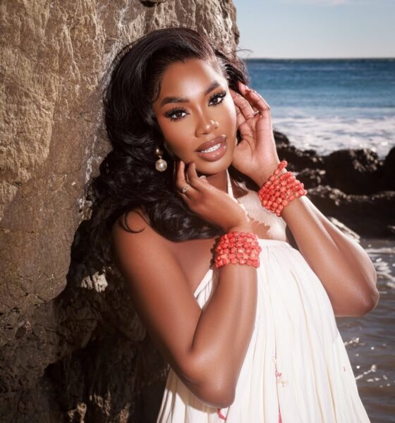 Close-up portrait of Sharon Ooja Nwoke leaning against a rock wall with coral beaded bracelets and a white Knanfe dress.