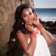 Close-up portrait of Sharon Ooja Nwoke leaning against a rock wall with coral beaded bracelets and a white Knanfe dress.