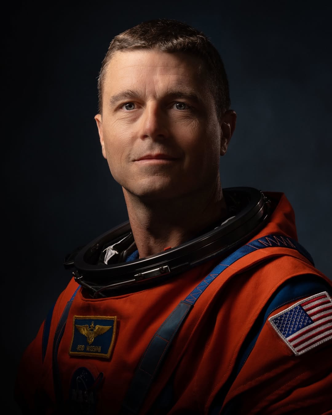 NASA astronaut Reid Wiseman in his orange Artemis flight suit featuring the U.S. flag and NASA meatball patches.