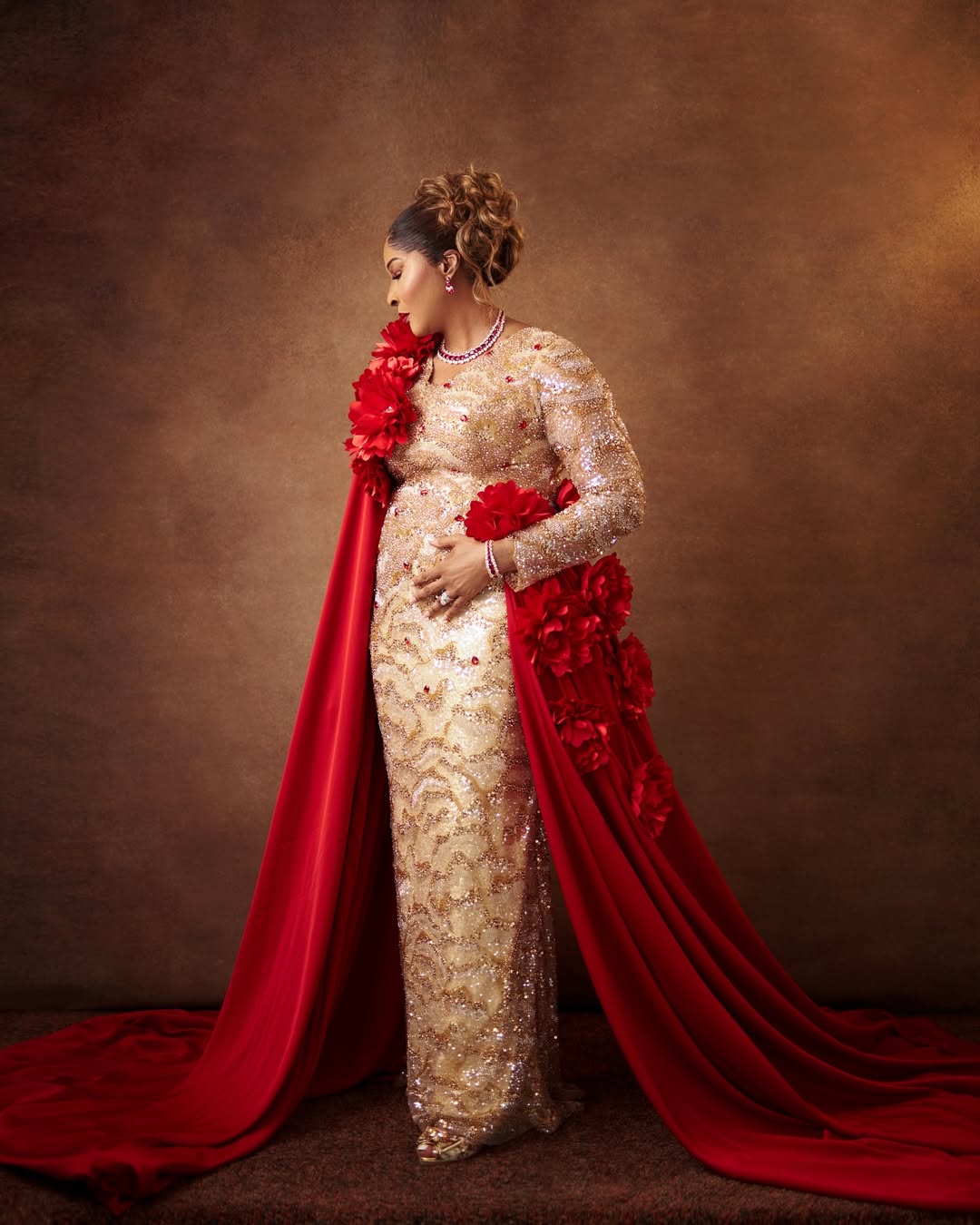 A 70-year-old celebrant in a champagne gold beaded gown with a dramatic red satin cape featuring 3D floral appliqués.