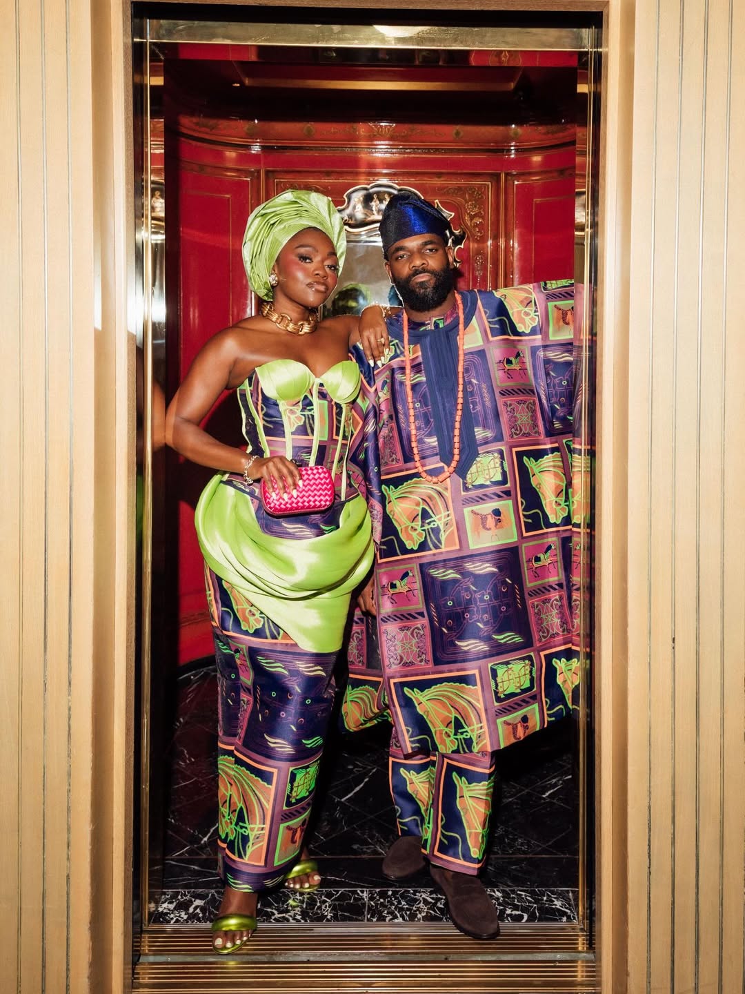 Fisayo Longe and Afolabi Mosuro standing in an elevator wearing matching neon lime-green and patterned silk traditional Nigerian wedding outfits.