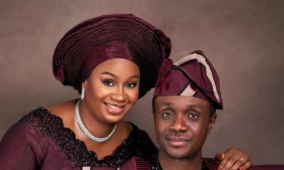 A close-up of Nigerian gospel minister Nathaniel Bassey and his wife Sarah holding hands, dressed in coordinated burgundy Yoruba traditional attire for their 13th wedding anniversary.