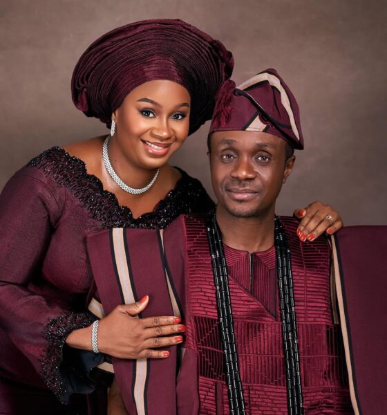 A close-up of Nigerian gospel minister Nathaniel Bassey and his wife Sarah holding hands, dressed in coordinated burgundy Yoruba traditional attire for their 13th wedding anniversary.