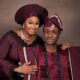 A close-up of Nigerian gospel minister Nathaniel Bassey and his wife Sarah holding hands, dressed in coordinated burgundy Yoruba traditional attire for their 13th wedding anniversary.