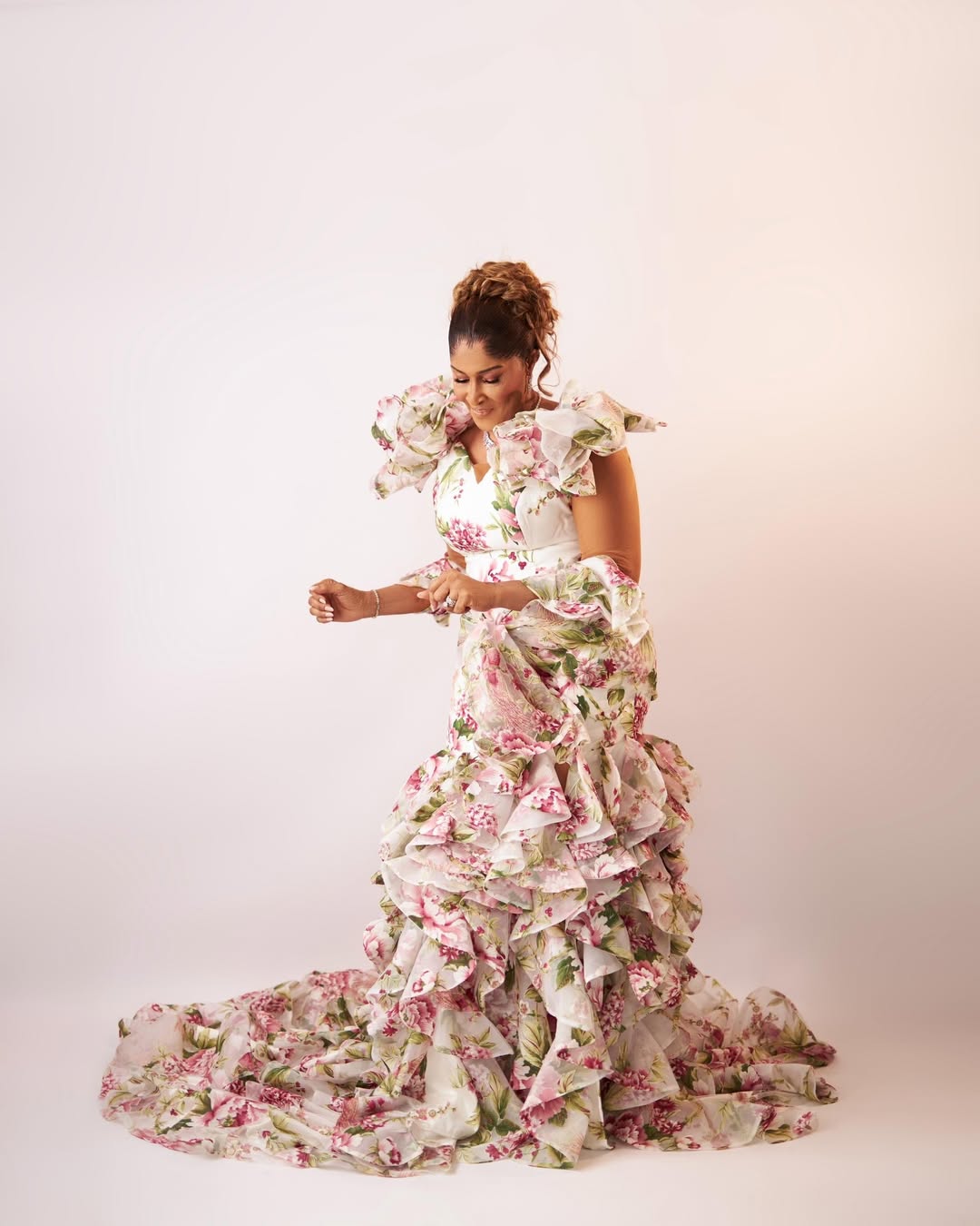 A portrait of a woman at 70 wearing a white mermaid gown with a pink botanical print and cascading organza ruffles, styled by Sorena Bridal.
