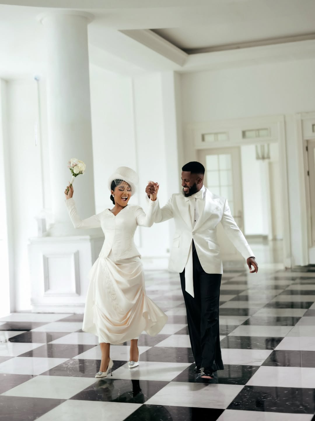 Akin Faminu and Kiky Festus dancing on a black and white checkered marble floor inside a bright hall during their civil wedding ceremony. Kiky wears a bespoke ivory two-piece bridal set by Mazelle Bridal and Akin is in a custom white dinner jacket by Deji and Kola.