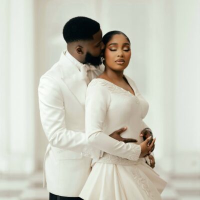 An intimate portrait of Akin Faminu embracing Kiky Festus from behind. Akin wears a white Deji and Kola dinner jacket; Kiky wears a bespoke ivory Mazelle Bridal two-piece set.