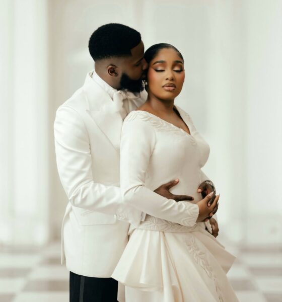 An intimate portrait of Akin Faminu embracing Kiky Festus from behind. Akin wears a white Deji and Kola dinner jacket; Kiky wears a bespoke ivory Mazelle Bridal two-piece set.