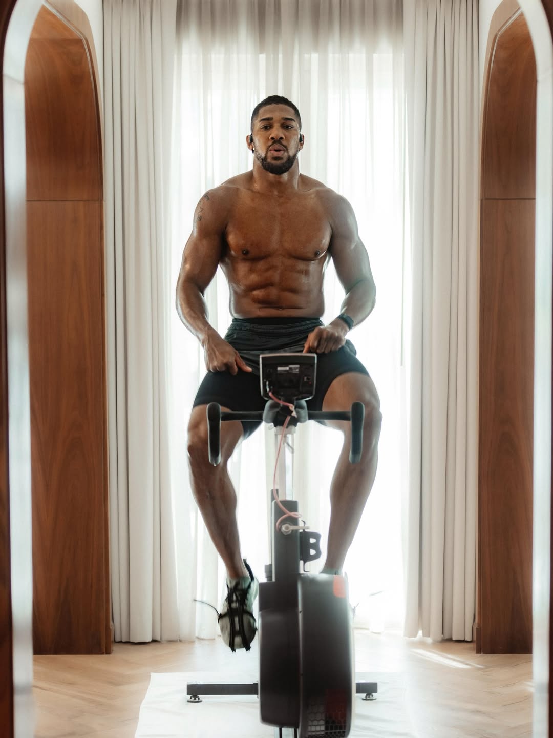 Anthony Joshua shirtless on an exercise bike during a high-intensity indoor training session.