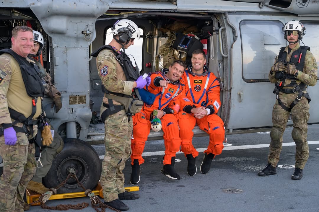 Artemis II commander Reid Wiseman and CSA astronaut Jeremy Hansen sitting on a Navy MH-60 Seahawk helicopter after being hoisted from the Pacific Ocean.