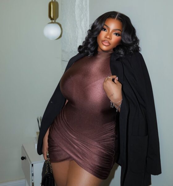 Dorathy Bachor wearing a chocolate brown mock-neck mini dress and a black blazer caped over her shoulders, holding a quilted leather clutch.