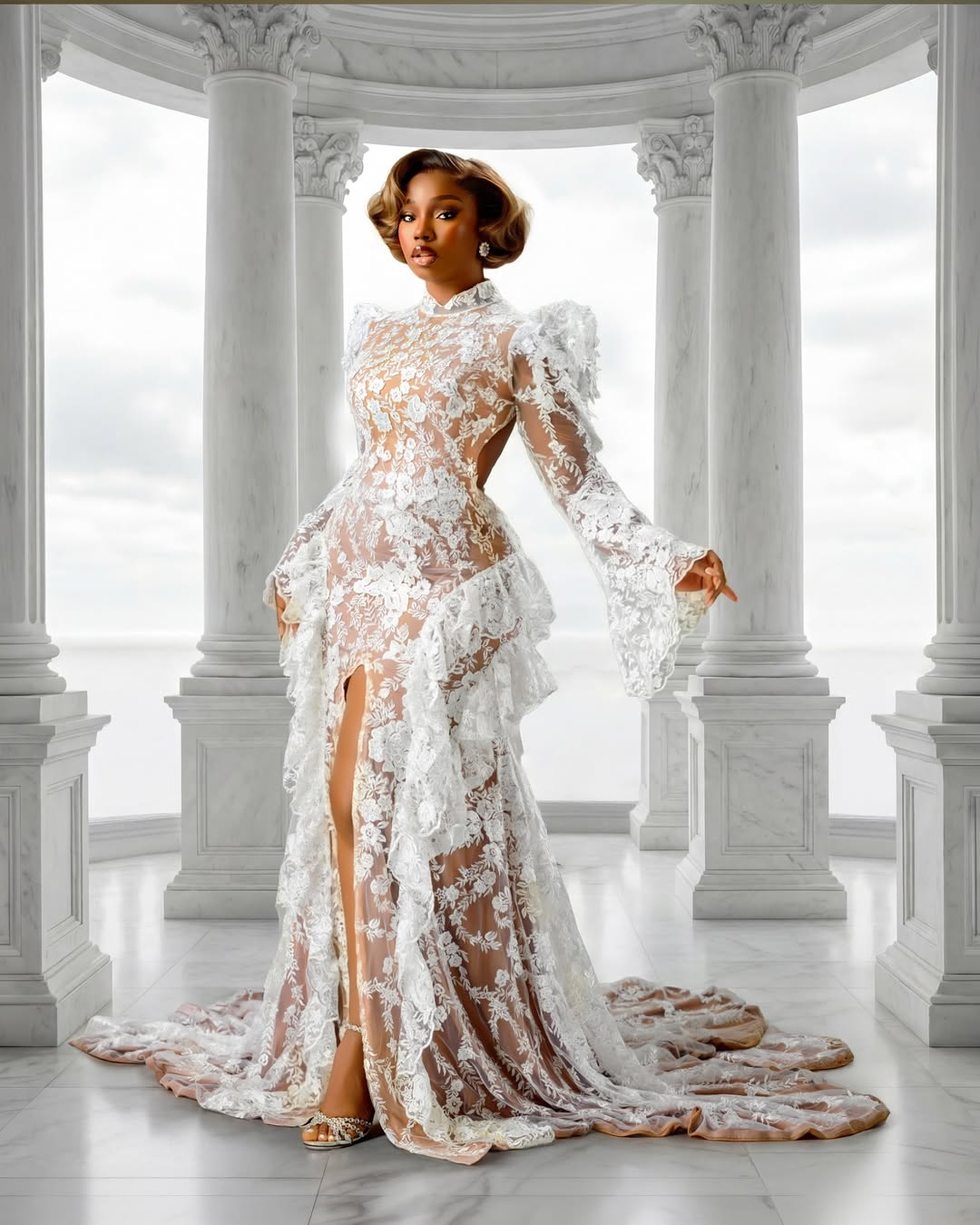 BamBam posing in a floor-length white lace gown by Medlin Couture with sculpted shoulders and bell cuffs, set against tall white marble columns.