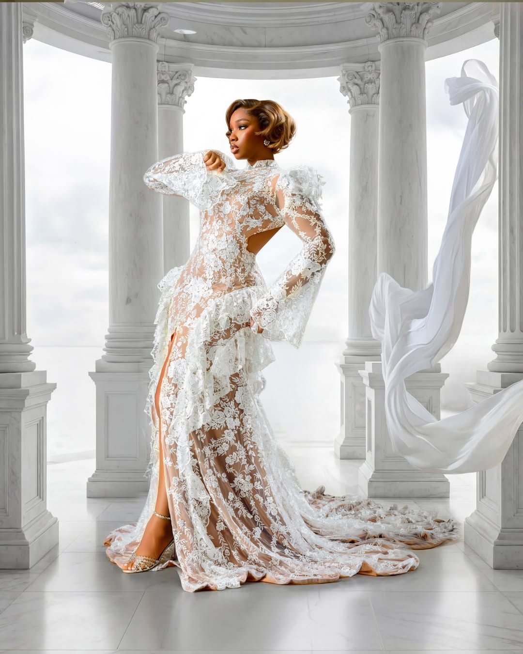 BamBam posing with one leg forward to reveal a front slit in her ruffled white lace skirt, highlighting her jewelled strappy heels.