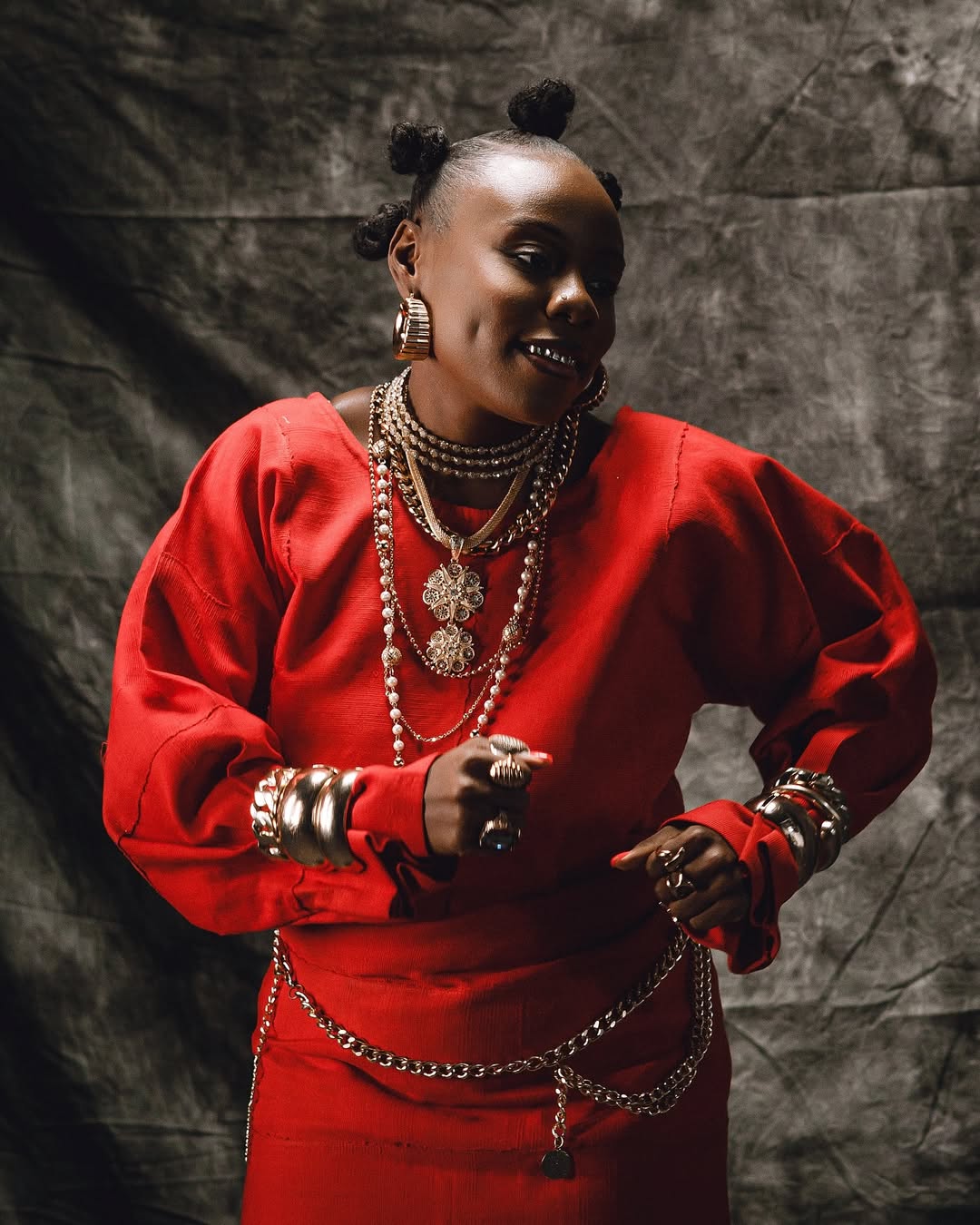 Close-up of Teni-the-Entertainer in red-clothing featuring layered-gold-necklaces and Bantu-knots hairstyle.