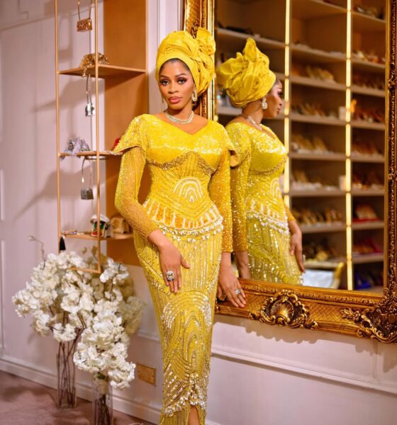 A portrait of Shade Okoya standing next to a gold-trimmed mirror, showing her reflection and the detail of her silver choker and drop earrings.
