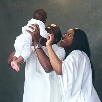Theophilus Sunday and Ashlee Sunday holding their son Mystery during a family photo session in all-white outfits.