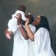 Theophilus Sunday and Ashlee Sunday holding their son Mystery during a family photo session in all-white outfits.