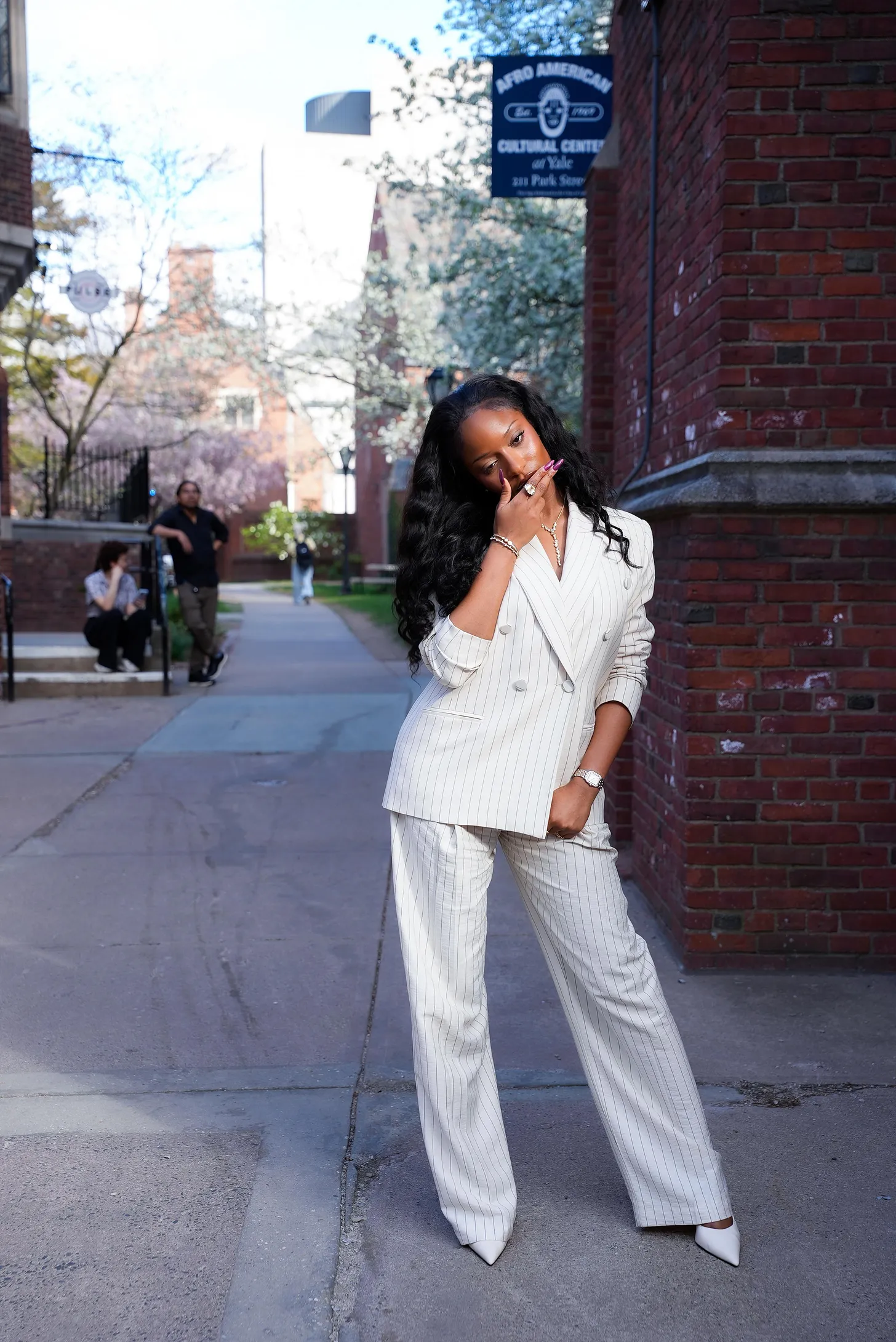 Ayra Starr posing outdoors at Yale University in a cream pinstripe suit ahead of the Africa Innovation Symposium.