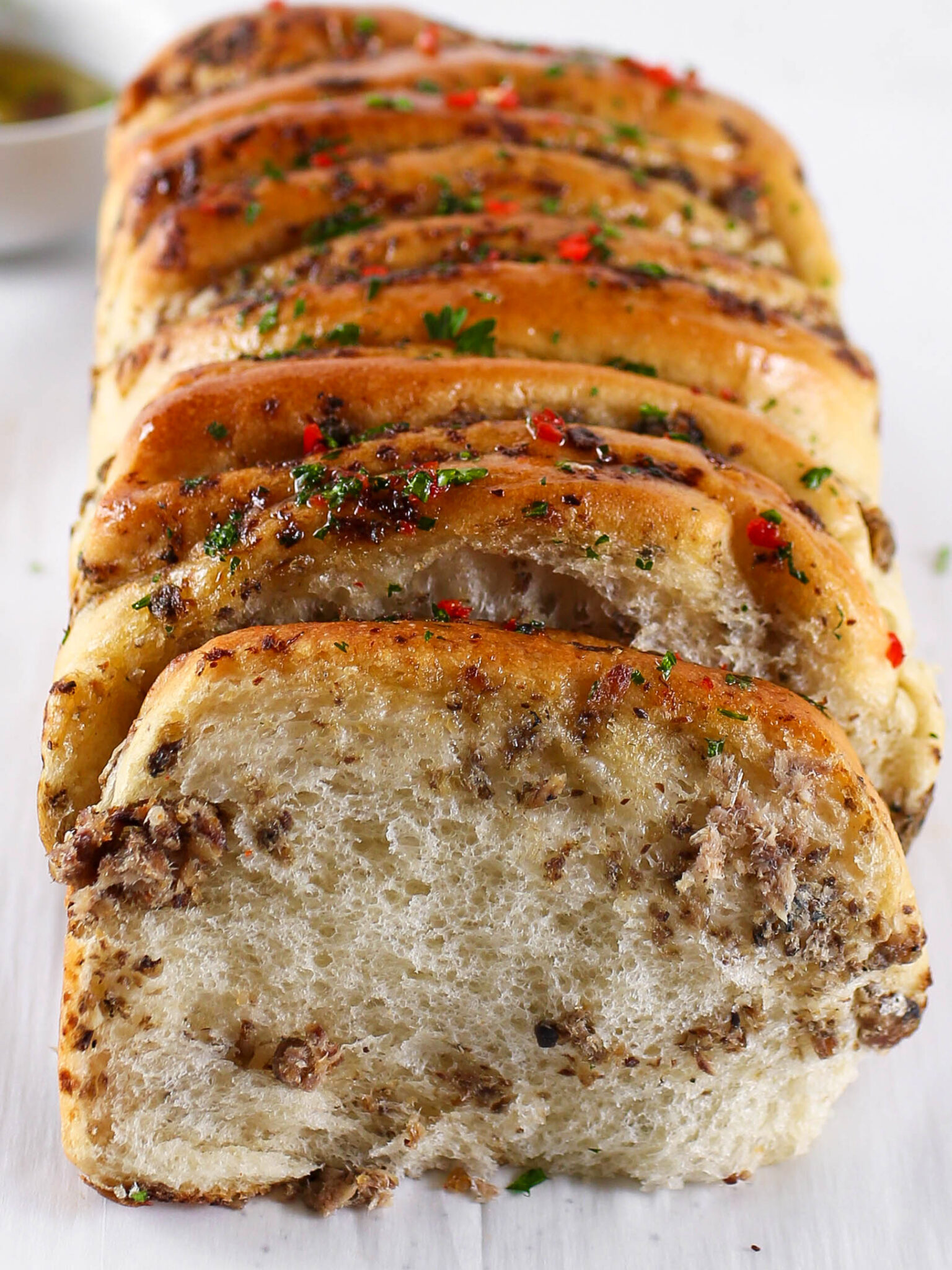 A close-up cross-section slice of Kikifoodies' baked sardine pull-apart bread, showing the soft, fluffy interior layers and savoury fish filling mixed with pepper flakes.