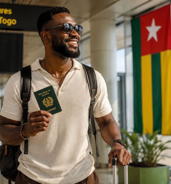An AI-generated photo of a smiling Ghanaian traveller holding an ECOWAS Ghana passport at Lomé-Gnassingbé Eyadéma International Airport, looking towards the large Togo flag on display in the departures terminal, representing Togo's new 30-day visa-free entry for African citizens.