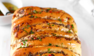 A golden-brown, freshly baked loaf of Kikifoodies' sardine pull-apart bread brushed with glossy, spicy oil and topped with chopped parsley and red pepper flakes.